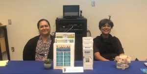 Two DCSS employees sitting behind a table with a blue tablecloth and brochures.